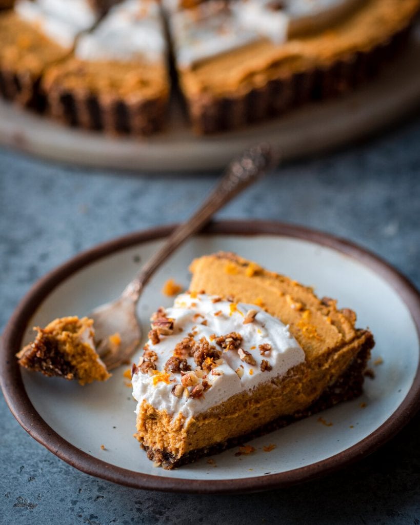 Slice of pumpkin tart and a fork on a grey plate on a grey table.
