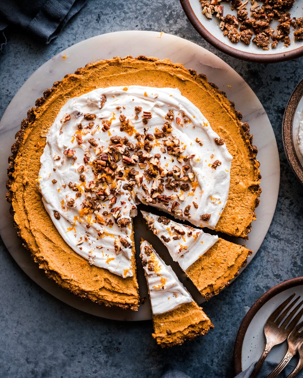 Sliced pumpkin cream tart on a marble platter on grey table.