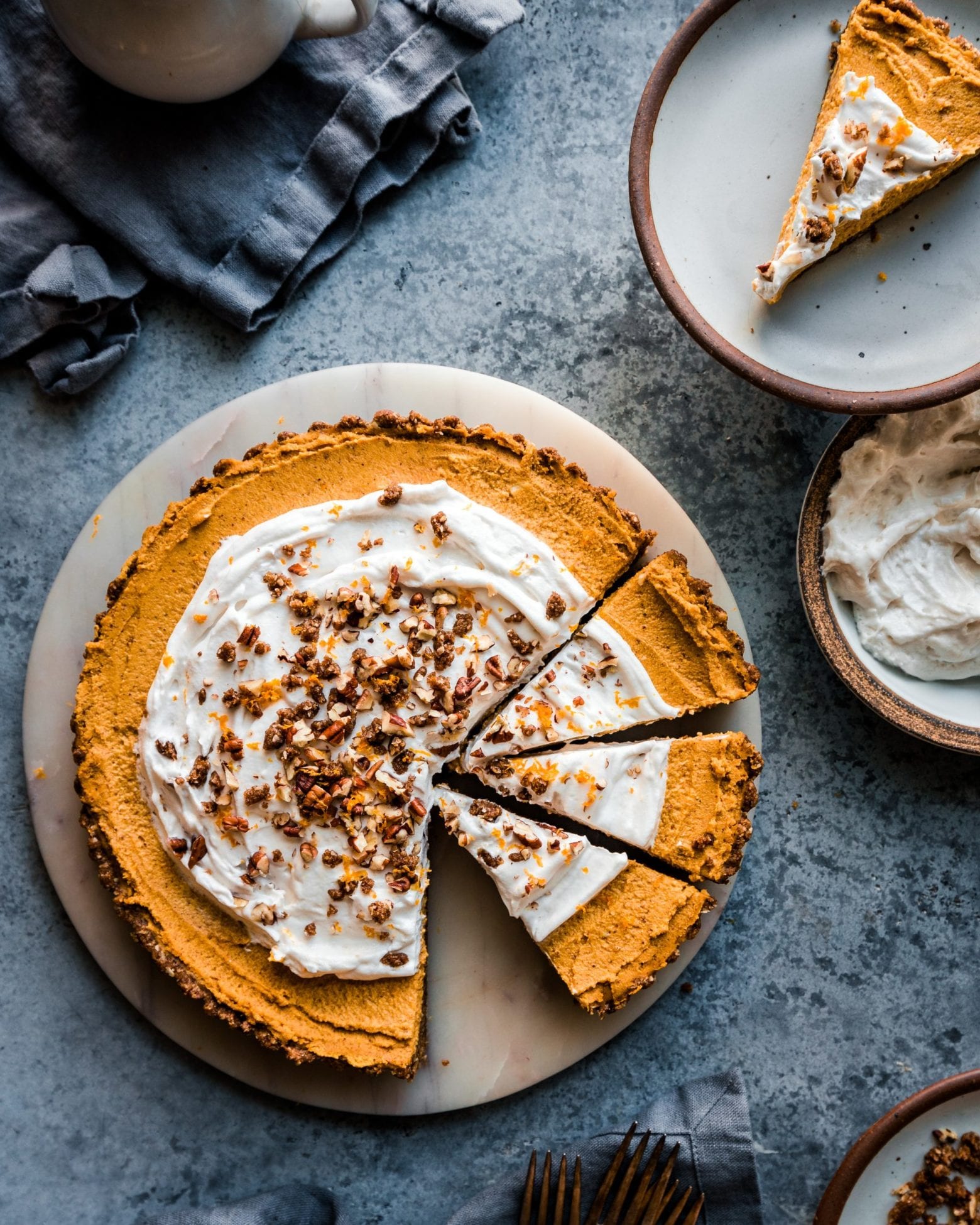 Pumpkin Cream Tart with three slices cut out on marble board on a grey table.