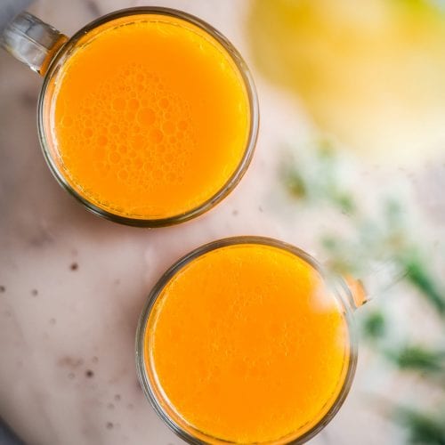 Overhead view of two glasses of turmeric tonic on a marble serving tray.