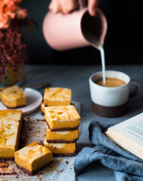 Woman pouring milk into mug next to cheesecake bars on a table.