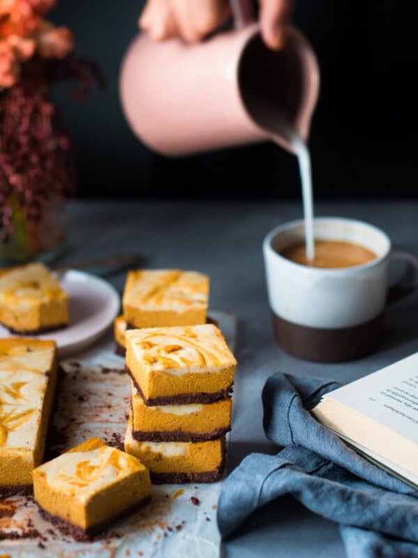 Woman pouring milk into mug next to cheesecake bars on a table.