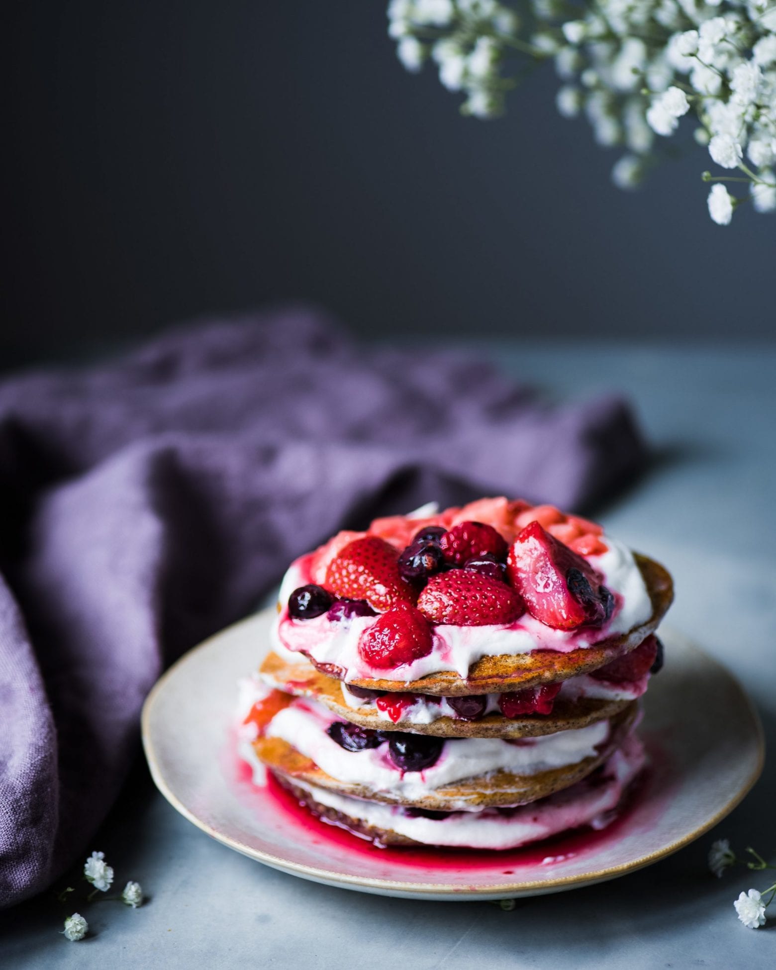 Grey plate stacked high with pancakes layered with vegan yogurt and berries.