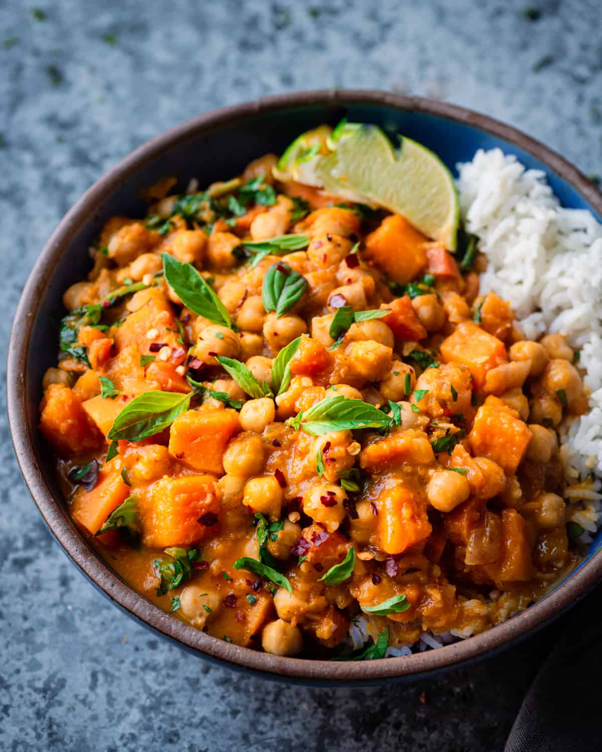 butternut squash curry with chickpeas in a blue cermamic bowl with Thai basil and white rice. 