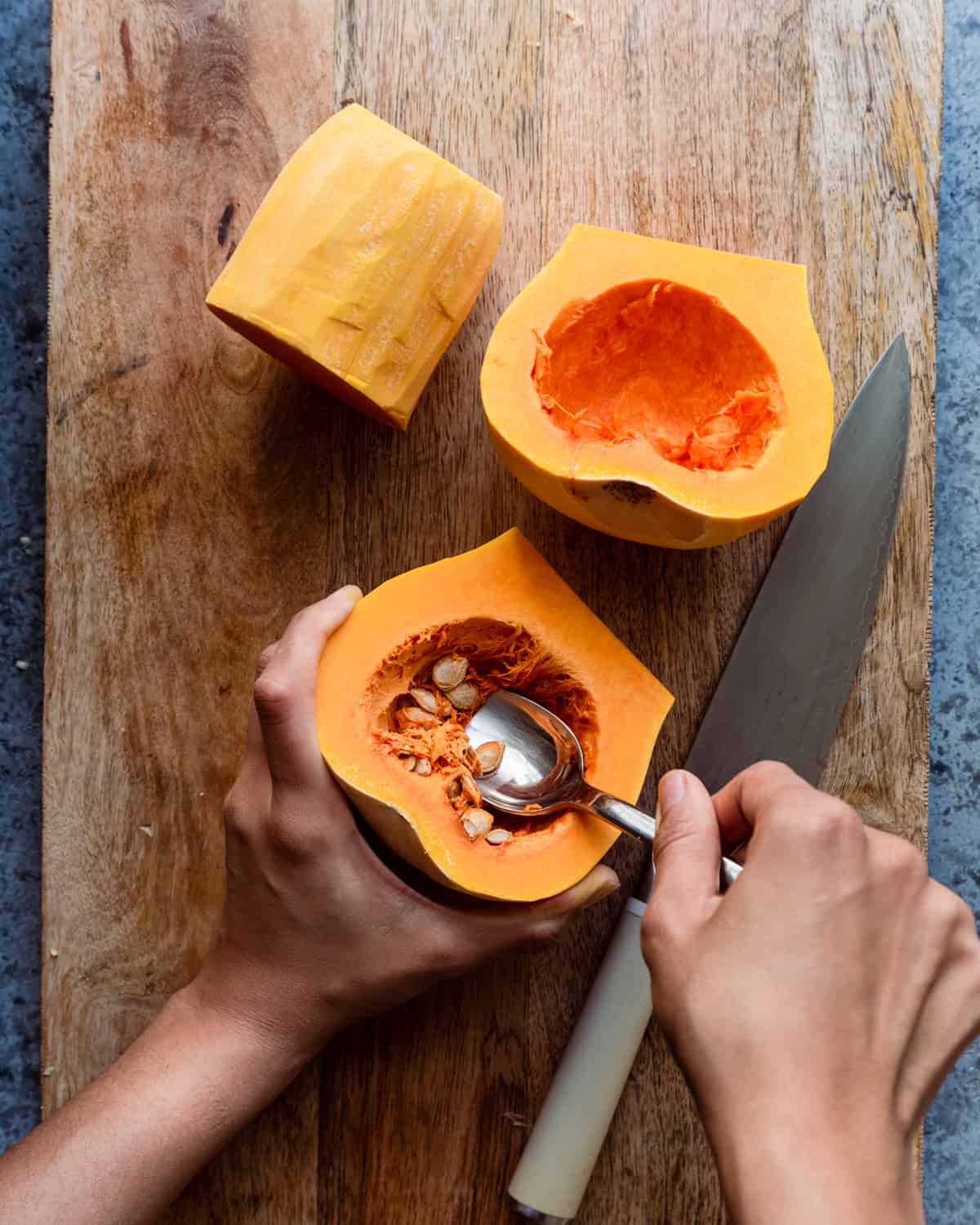 woman's hands scooping out seeds from butternut squash cavity on cutting board.