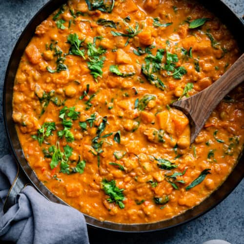 butternut squash curry with chickpeas and greens in a black pan with spoon dug into the curry.