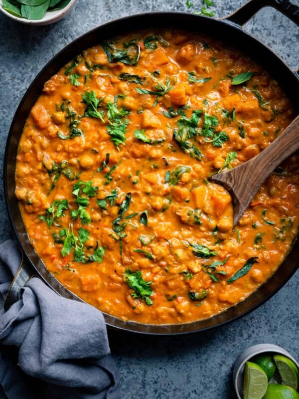 butternut squash curry with chickpeas and greens in a black pan with spoon dug into the curry.