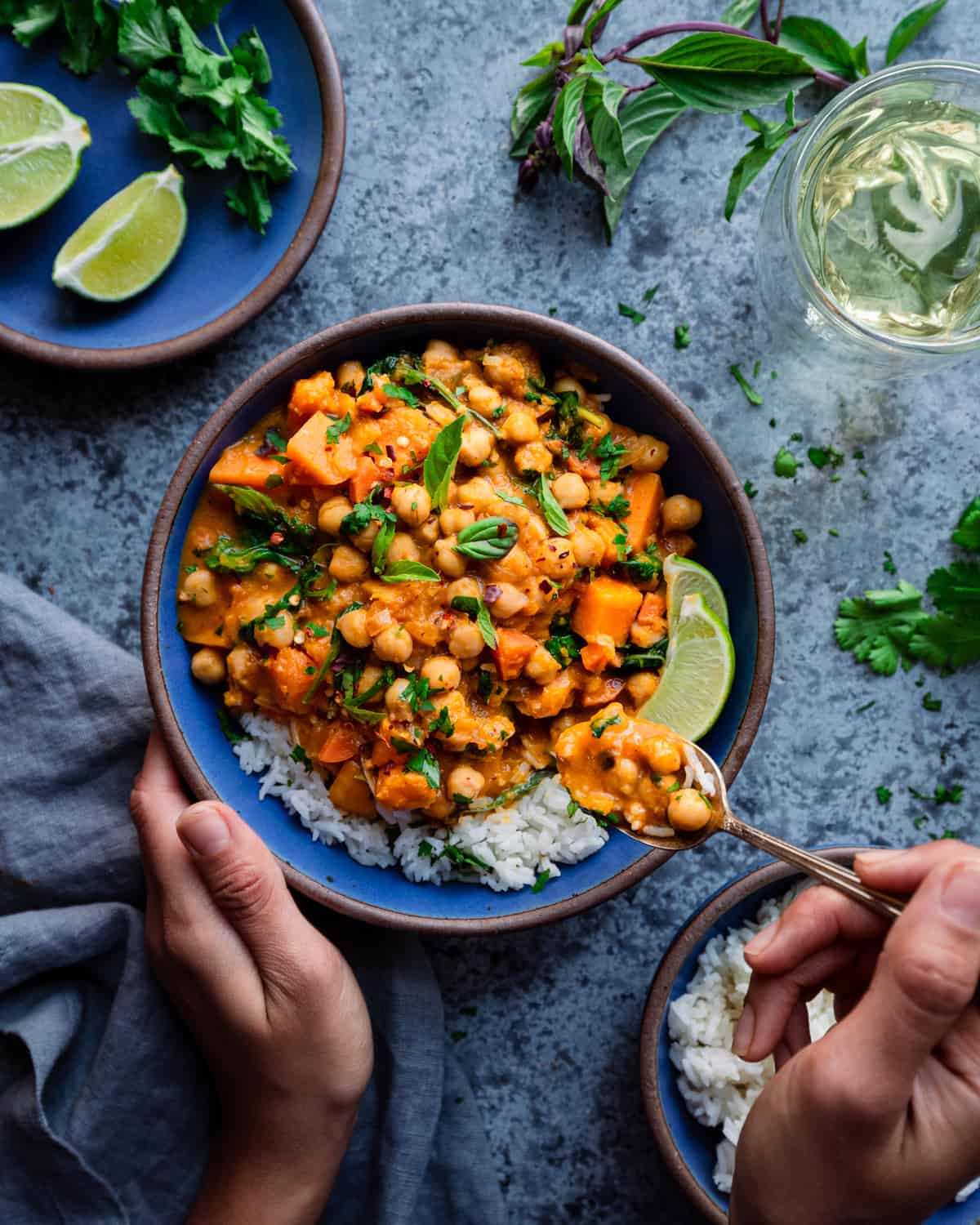woman's hands digging into a butternut squash curry with a spoon on a blue table. 
