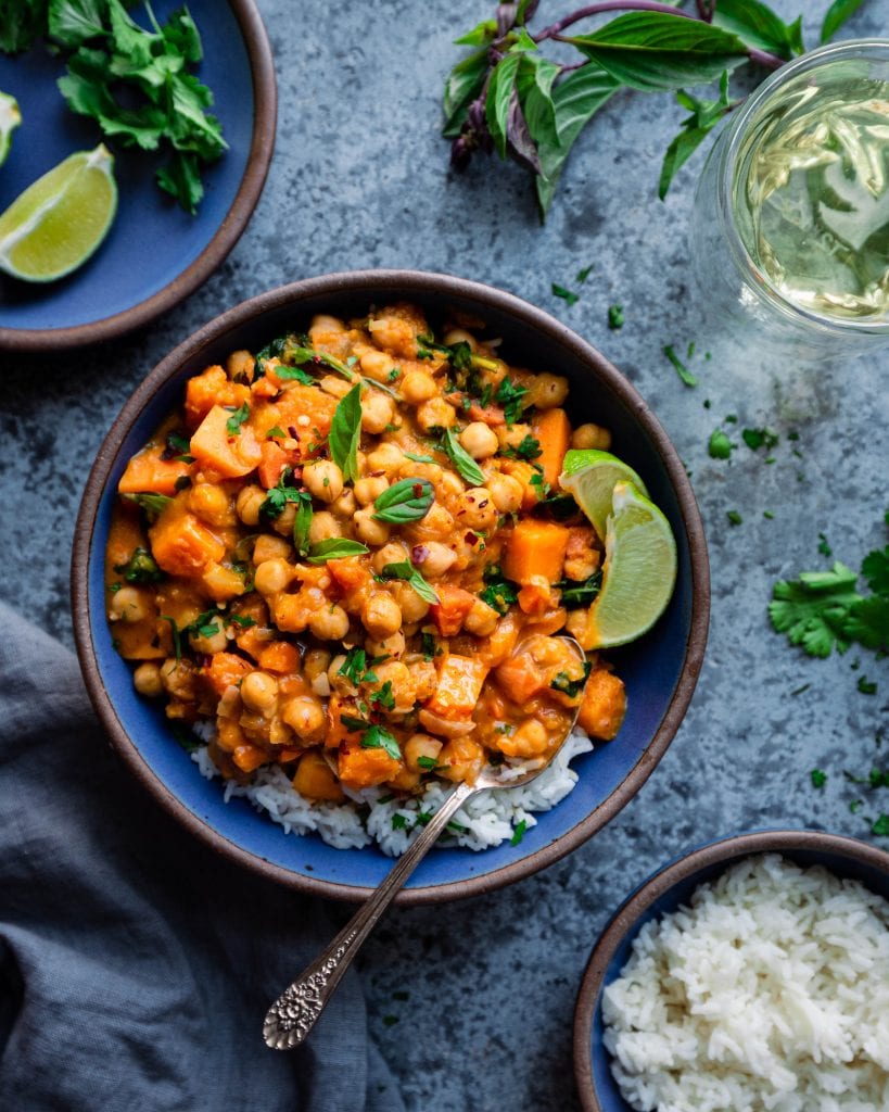 chickpea curry with rice and lime on blue board with glass of wine