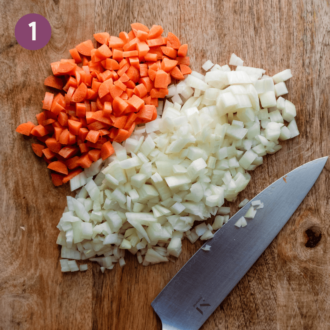 diced carrots and onions on a wooden cutting board with a knife.
