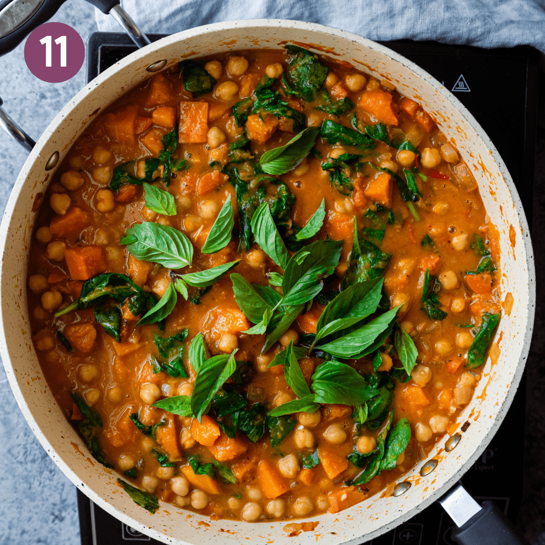 thai basil sitting on top of a butternut squash curry with chickpeas in a saute pan. 