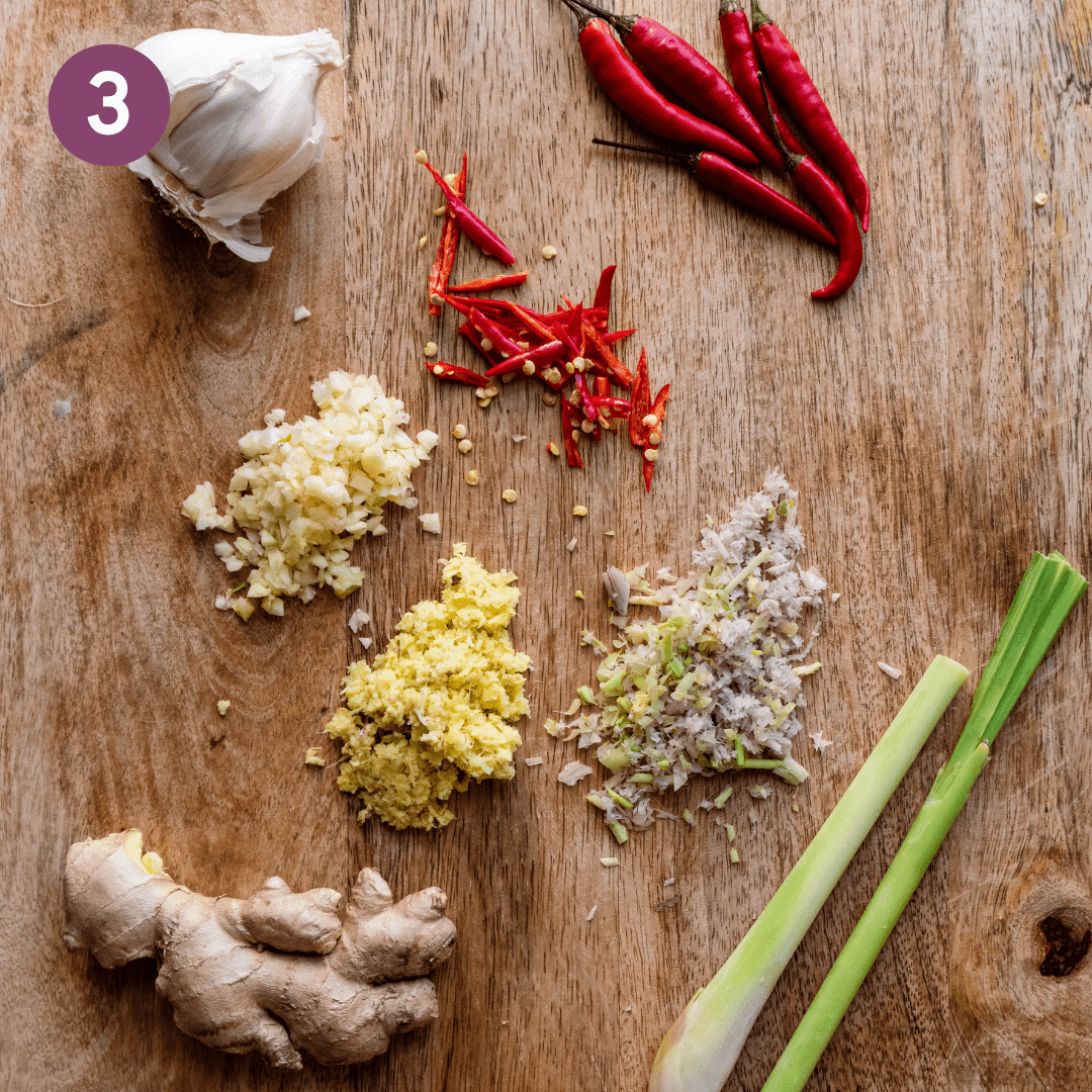 lemongrass, ginger, garlic, and thai chile peppers prepped on a cutting board. 