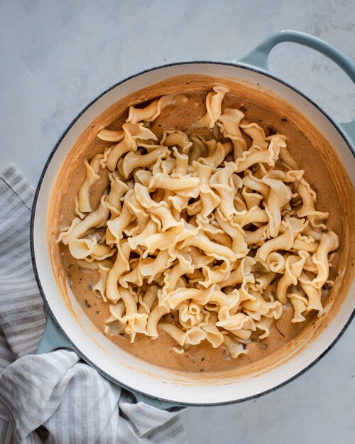 pasta being poured on top of stroganoff sauce