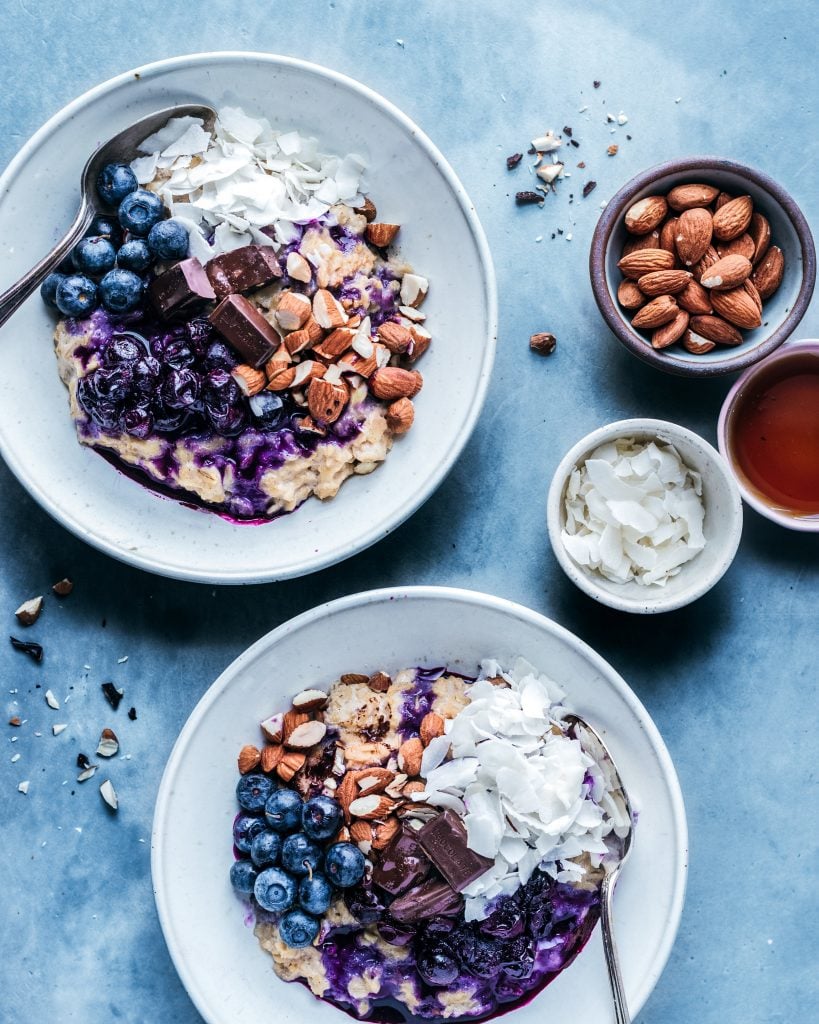 bowls of oatmeal with stewed blueberries, almonds, and coconut