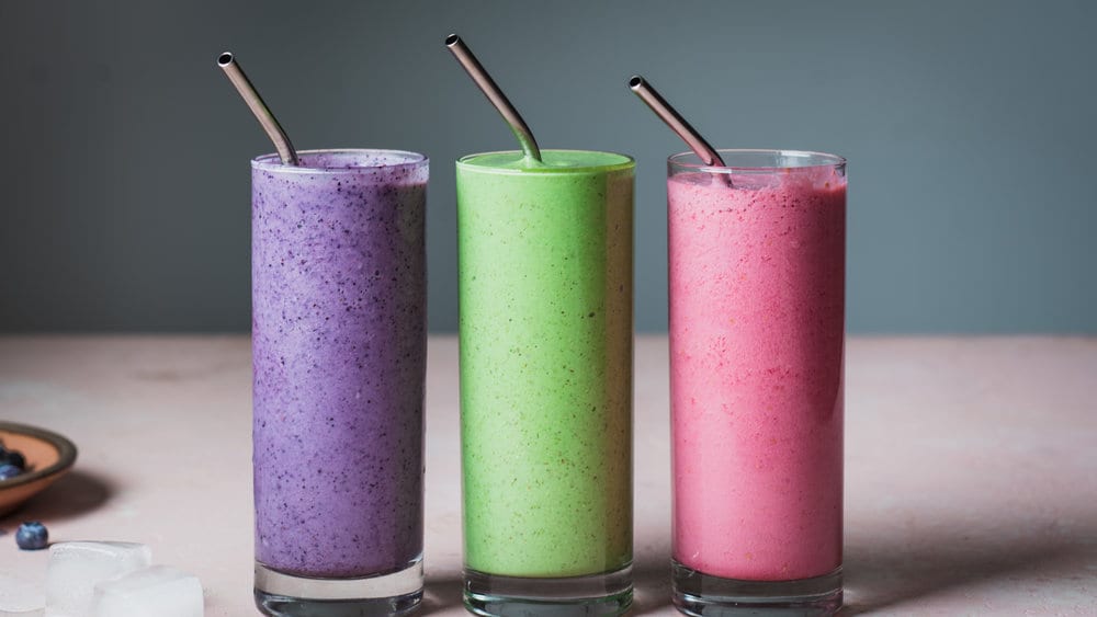 Three smoothies with stainless steel straws in glasses on a table.