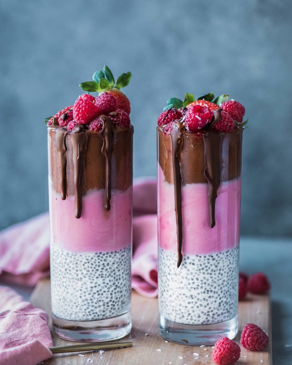 Two chocolate, raspberry and chia seed smoothies topped with raspberries on a wooden cutting board.