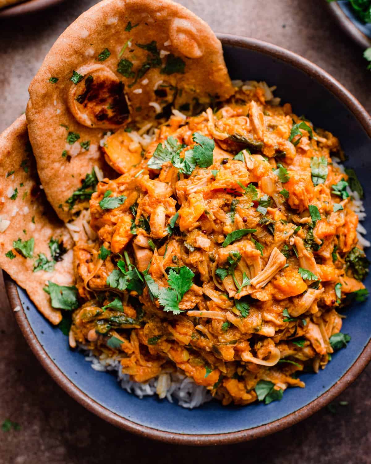 vegan jackfruit curry over rice in blue bowl with whole wheat naan