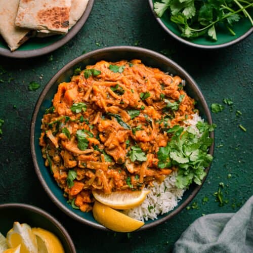 vegan jackfruit curry in green bowl with cilantro, lemon and naan on the side