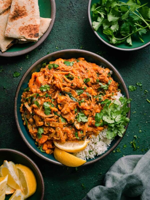 vegan jackfruit curry in green bowl with cilantro, lemon and naan on the side