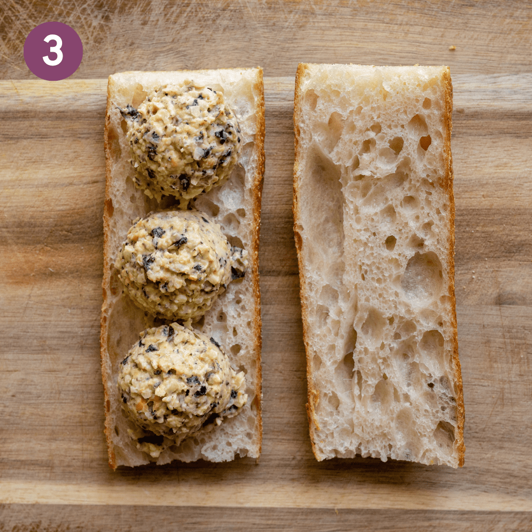 three scoops of vegan tuna salad on a baguette on a wooden cutting board.