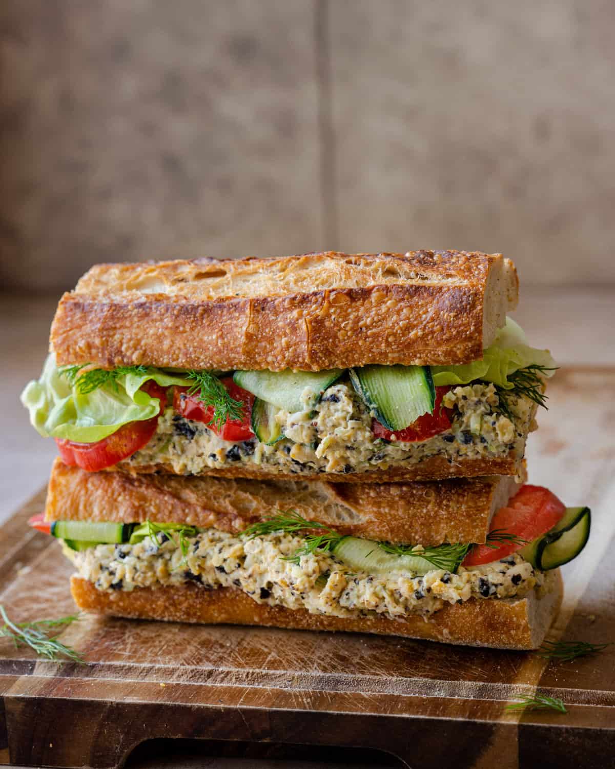 two baguette sandwiches stuffed with vegan tuna salad, cucumber, lettuce and tomato on wooden board. 