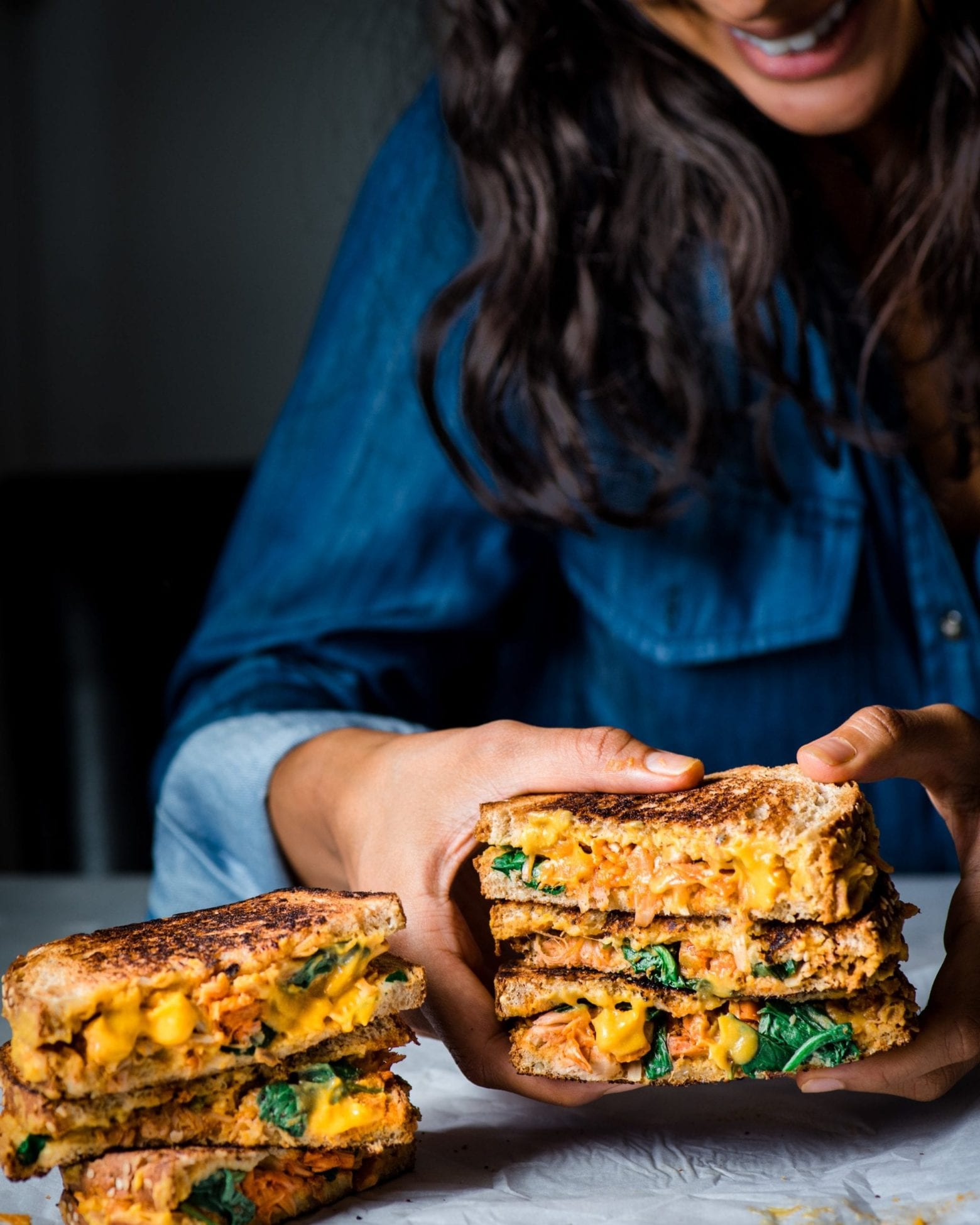 Woman holding cut in half vegan grilled cheese sandwich over a table.