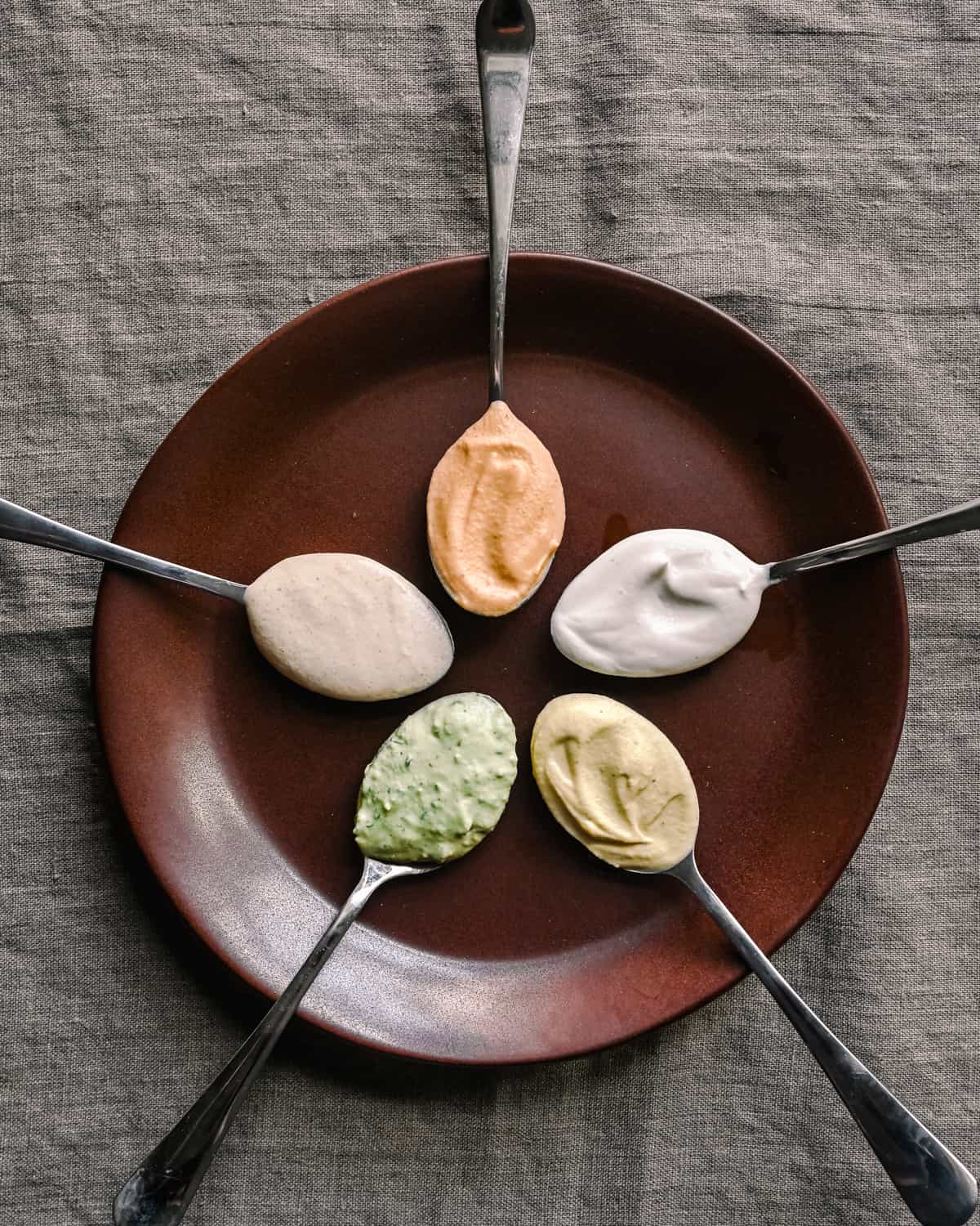 five flavor variations of cashew cream on spoons sitting on brown plate