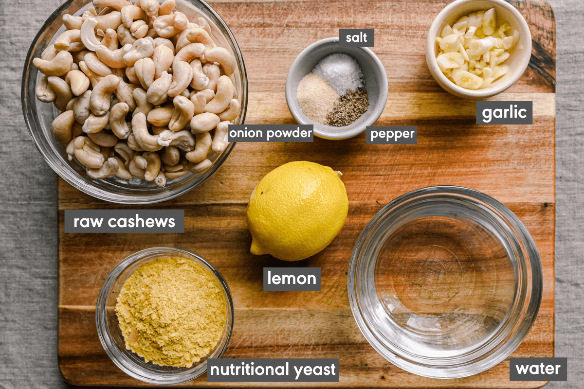 labeled ingredients on wooden cutting board with cashews, lemons, water, nutritional yeast