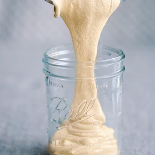 pouring cashew cream from blender into glass mason jar