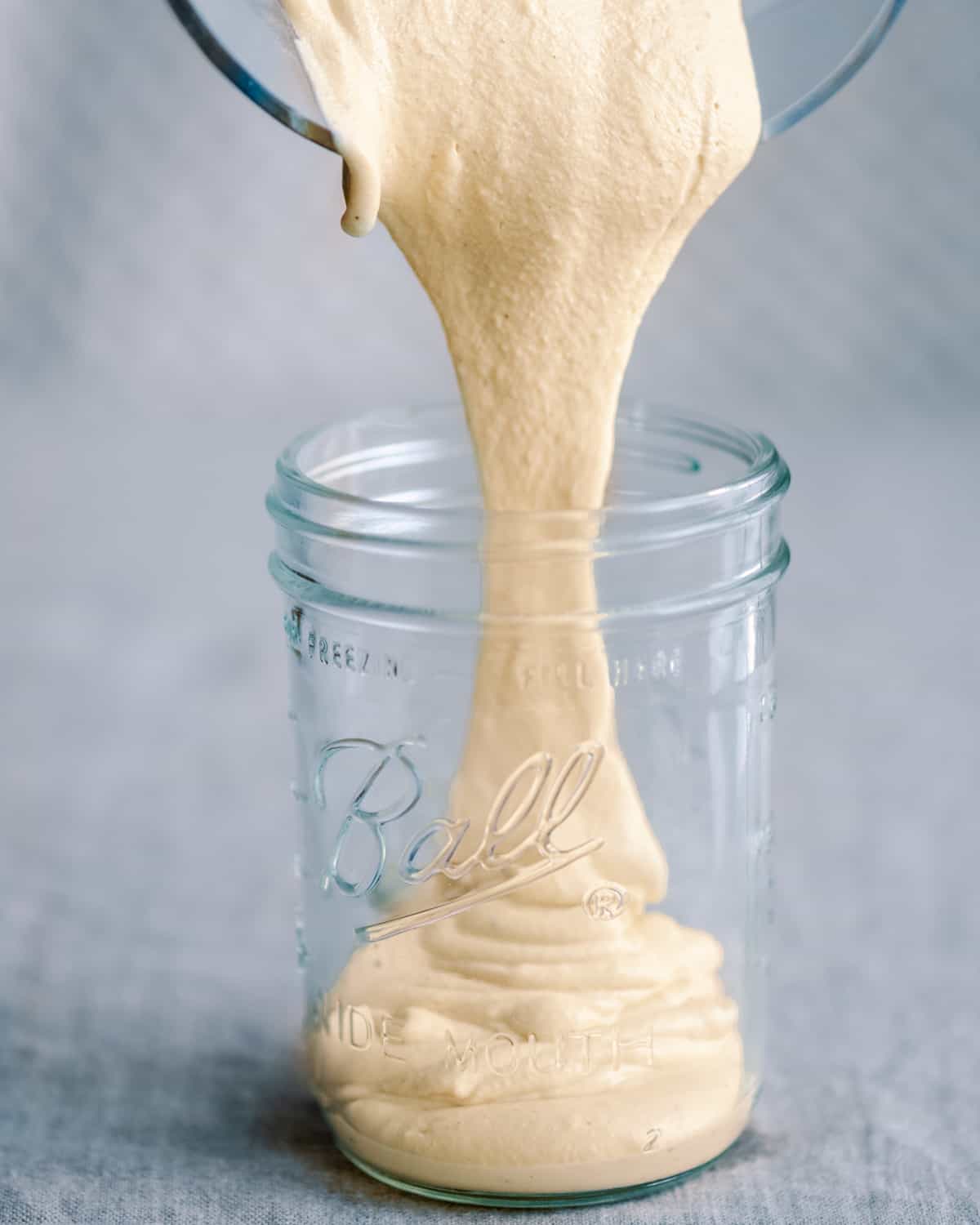 pouring cashew cream from blender into glass mason jar
