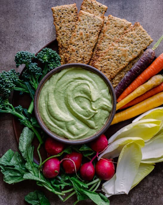 bowl of cilantro cashew cream dip on plate with colorful crudites and crackers