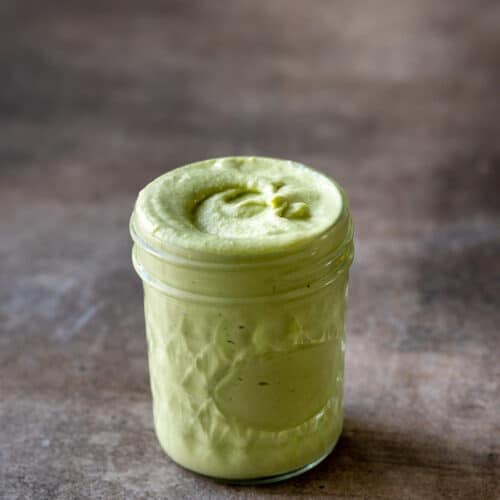 Cilantro cashew cream in glass jar on brown table.