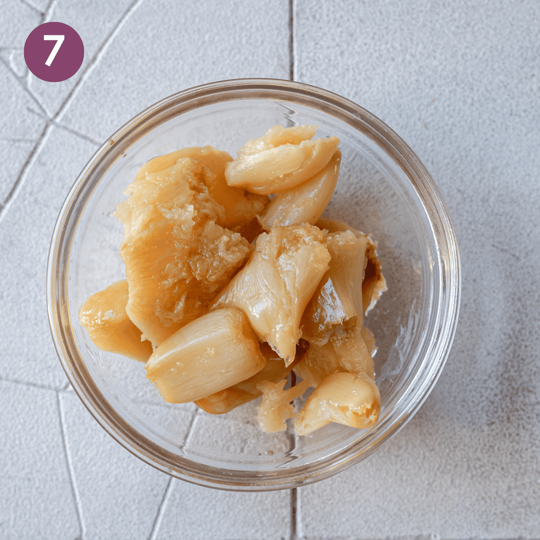 roasted garlic cloves in a glass bowl on a tiled surface. 