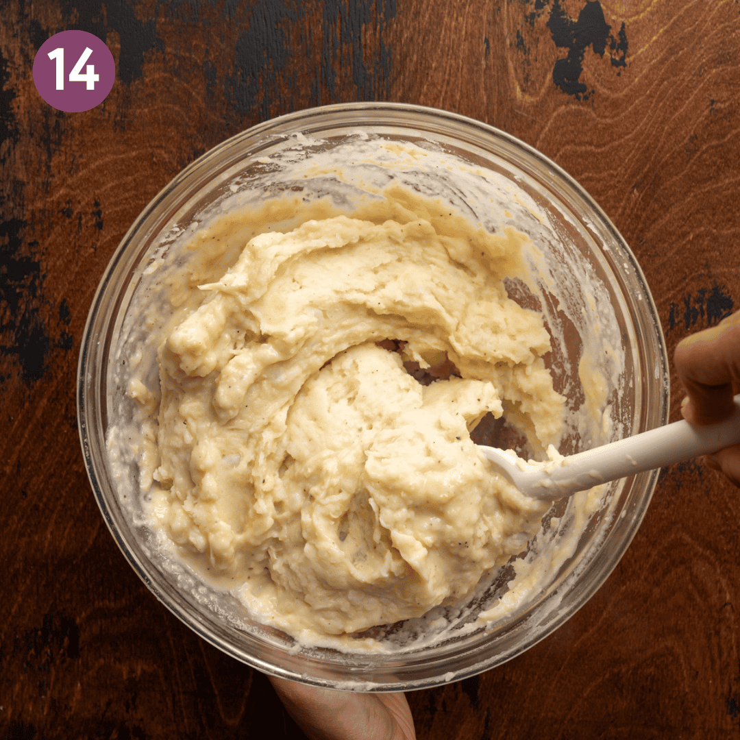 silicone spatula folding creamy mashed potatoes together in a glass bowl.