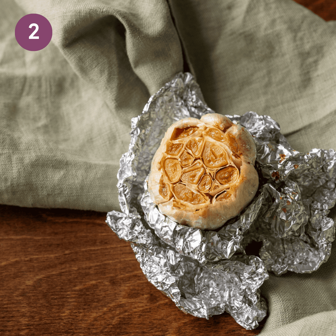 a head of golden roasted garlic wrapped in aluminum foil. 