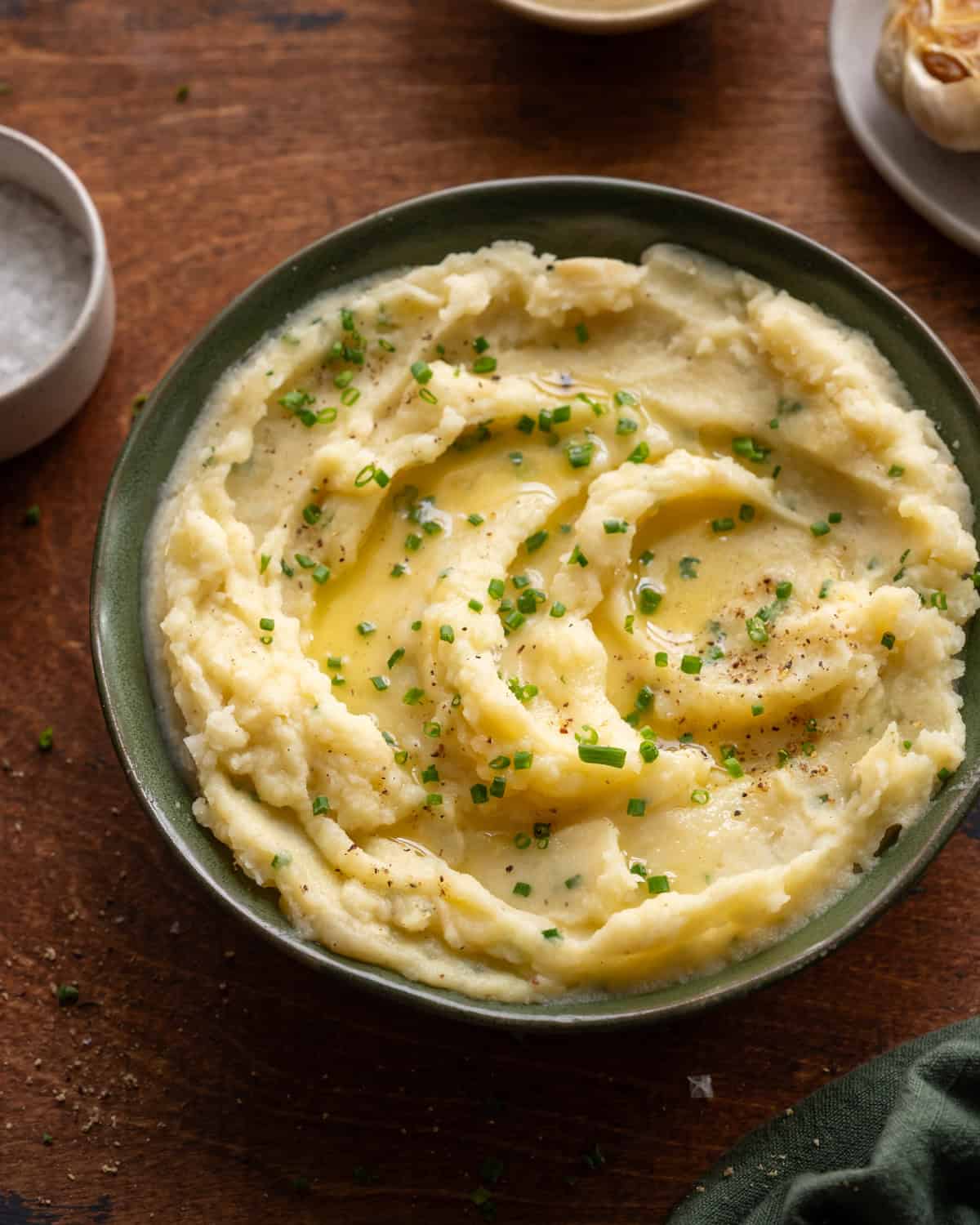 angled shot of a bowl of mashed potatoes with melted butter on a wooden table. 