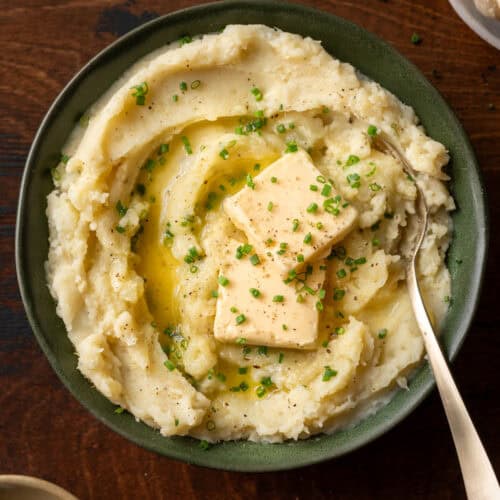 a bowl of fluffy mashed potatoes with two pats of butter and chives in green bowl.