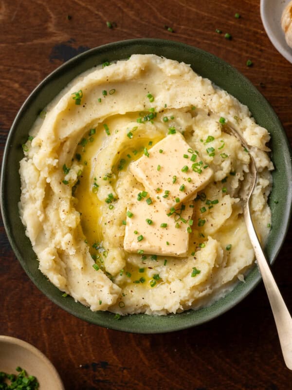a bowl of fluffy mashed potatoes with two pats of butter and chives in green bowl.