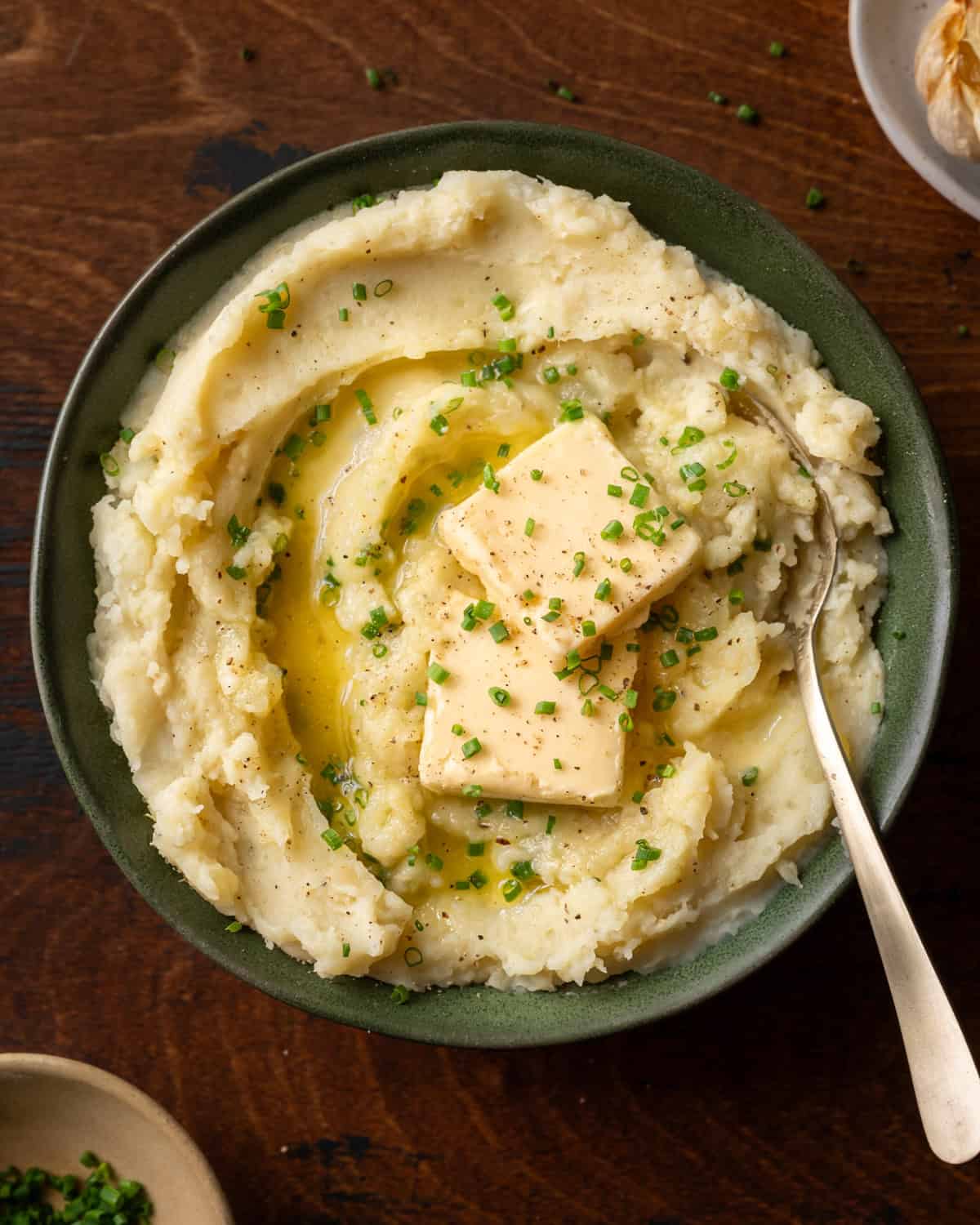 a bowl of fluffy mashed potatoes with two pats of butter and chives in green bowl.