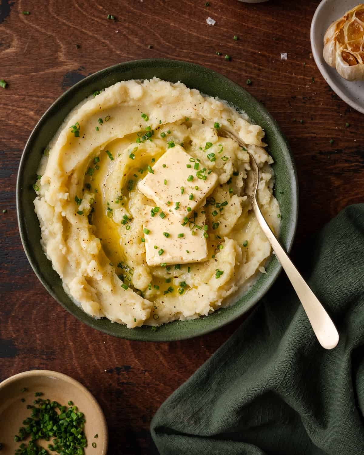 a bowl of fluffy mashed potatoes with two pats of butter and chives in green bowl.