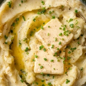 super closeup shot of fluffy mashed potatoes with pats of butter and chives on top.