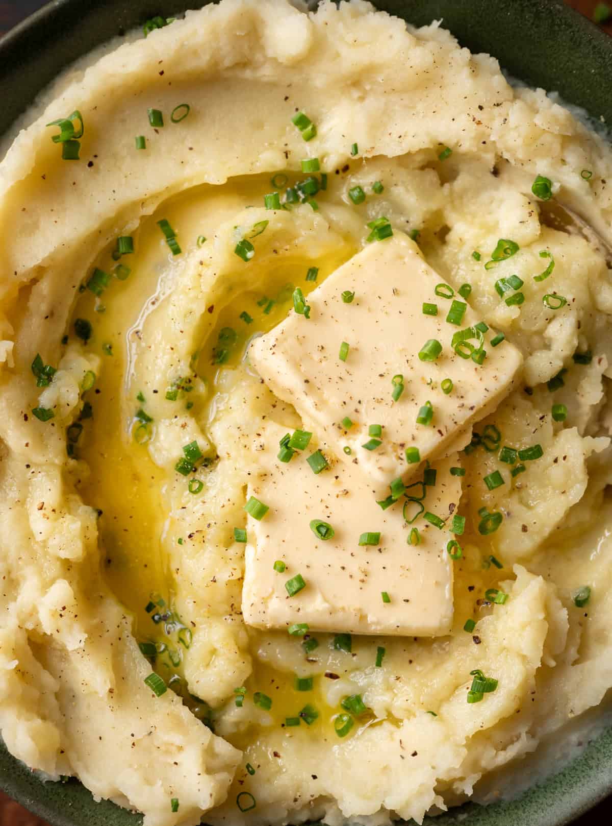 super closeup shot of fluffy mashed potatoes with pats of butter and chives on top.