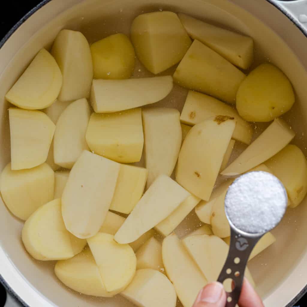 adding salt to chopped potatoes in saucepan full of water