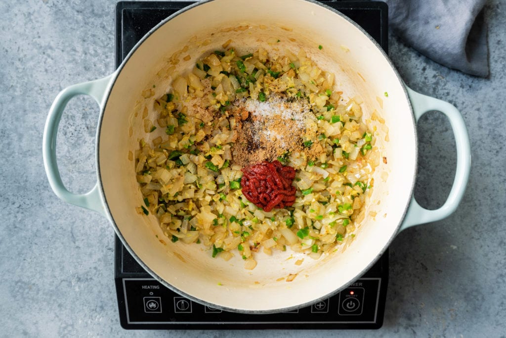 adding tomato paste and spices to sauteed aromatics in dutch oven