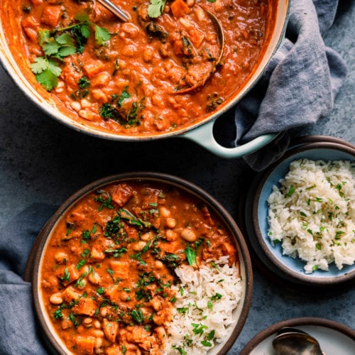 Bowl of west african peanut stew on table with dutch oven with peanut stew and bowl of rice