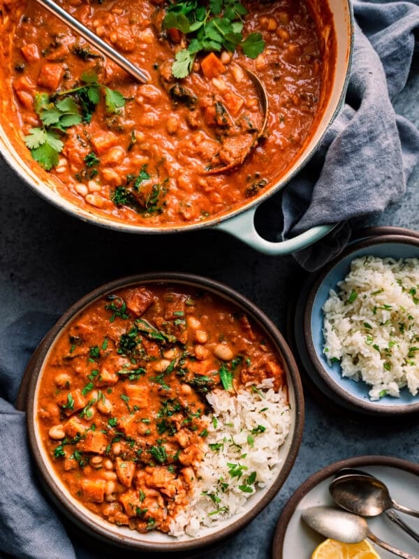 Bowl of west african peanut stew on table with dutch oven with peanut stew and bowl of rice