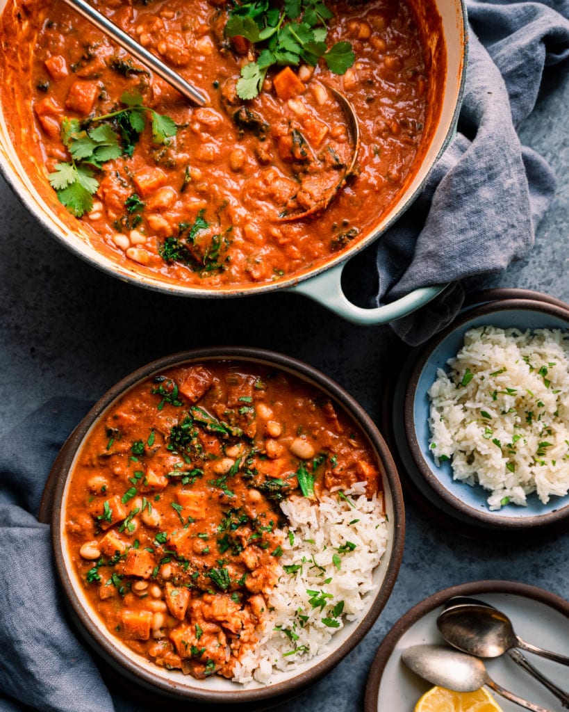 Bowl of west african peanut stew on table with dutch oven with peanut stew and bowl of rice