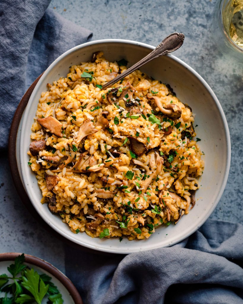 vegan mushroom risotto in ceramic bowl with spoon, napkin, and wine