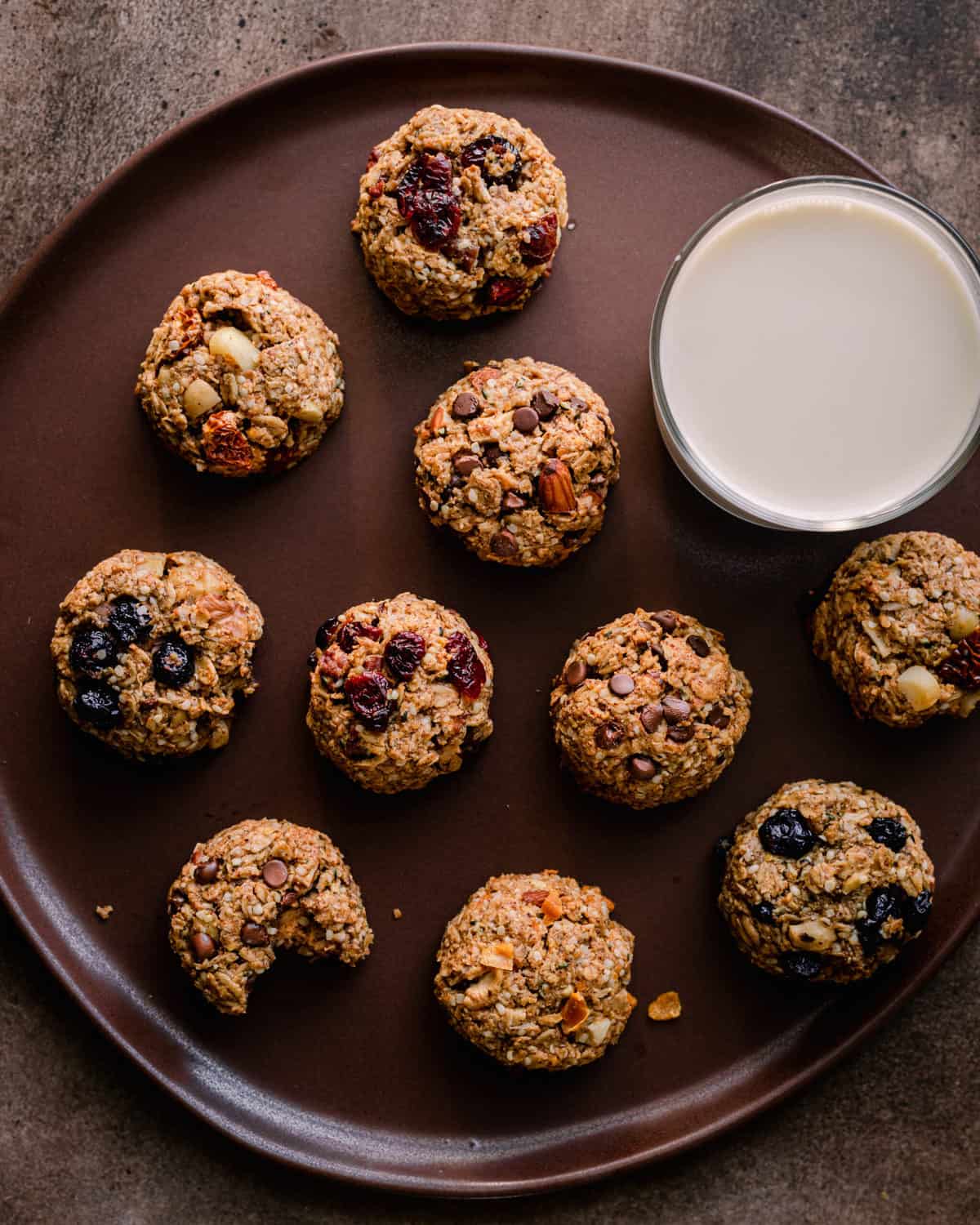 brown plate of breakfast cookies with one bitten into and a glass of oat milk