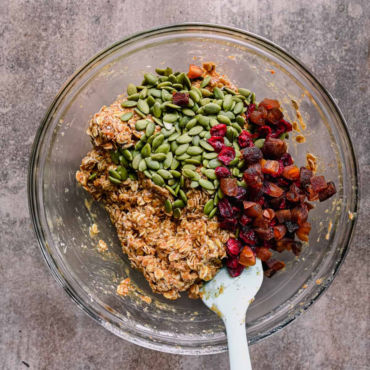 pepitas and dried fruit on top of cookie dough in bowl.